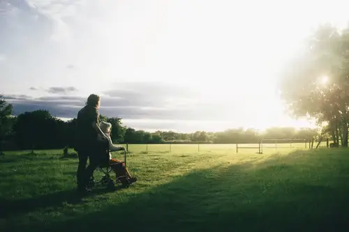 Aidant accompagnant une personne âgée en fauteuil roulant en ballade dans un champ lors du lever de soleil